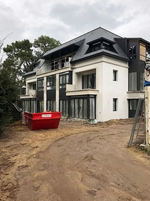 Chantier de construction en phase de finition extérieure, bâtiment R+2 avec toiture en ardoise, façade mixte blanc et bardage sombre, menuiseries noires