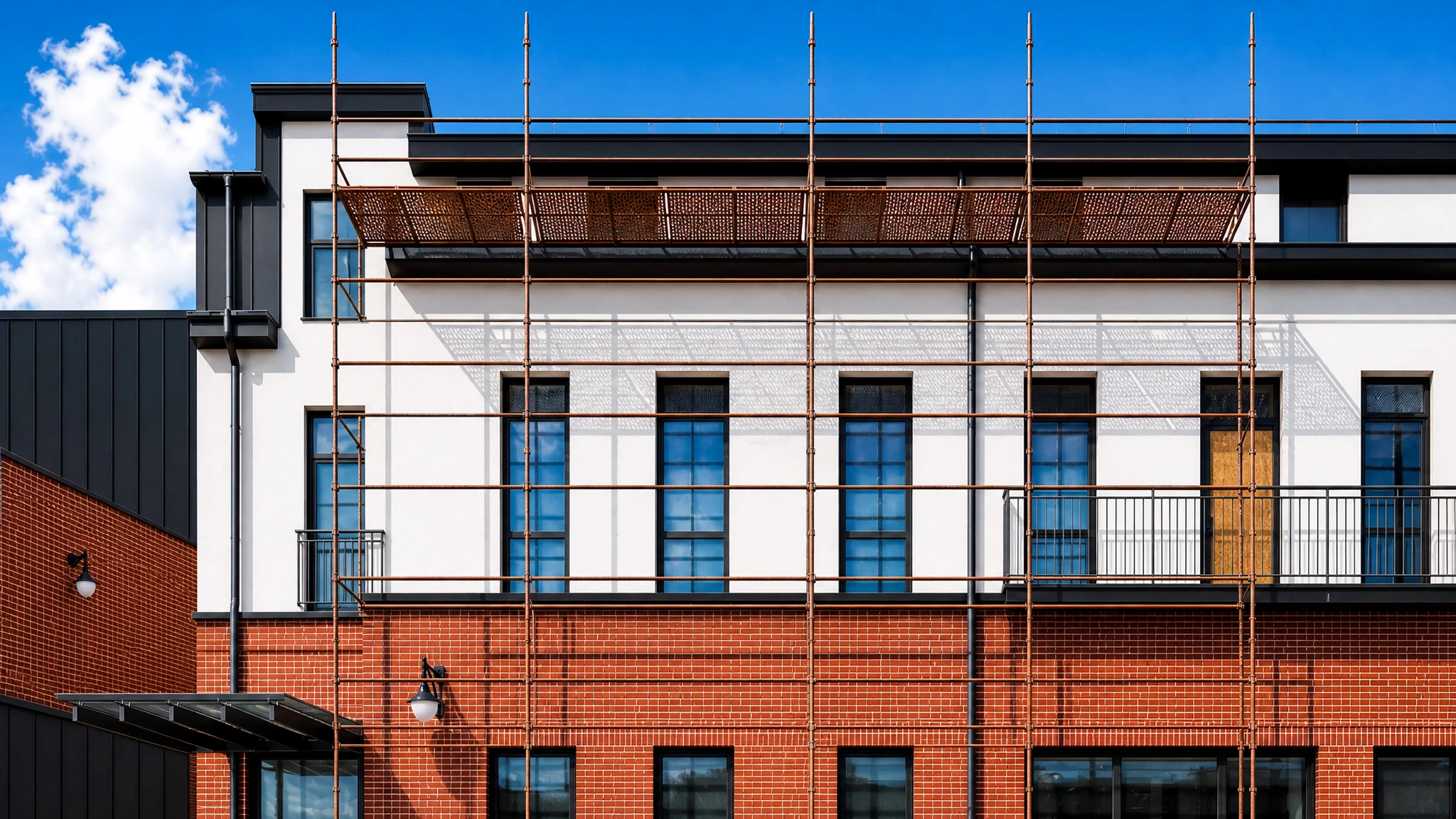 Chantier extérieur d'une villa contemporaine en cours de rénovation, façade bicolore blanc et noir, toiture ardoise avec lucarnes, balcons à garde-corps métalliques ajourés